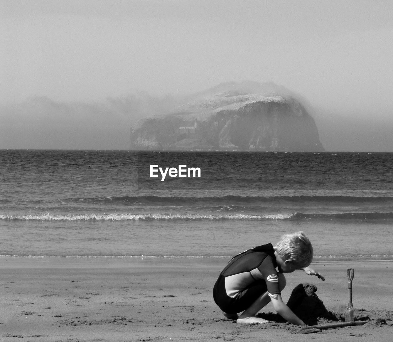 Boy making sandcastle at beach against bass rock in sea