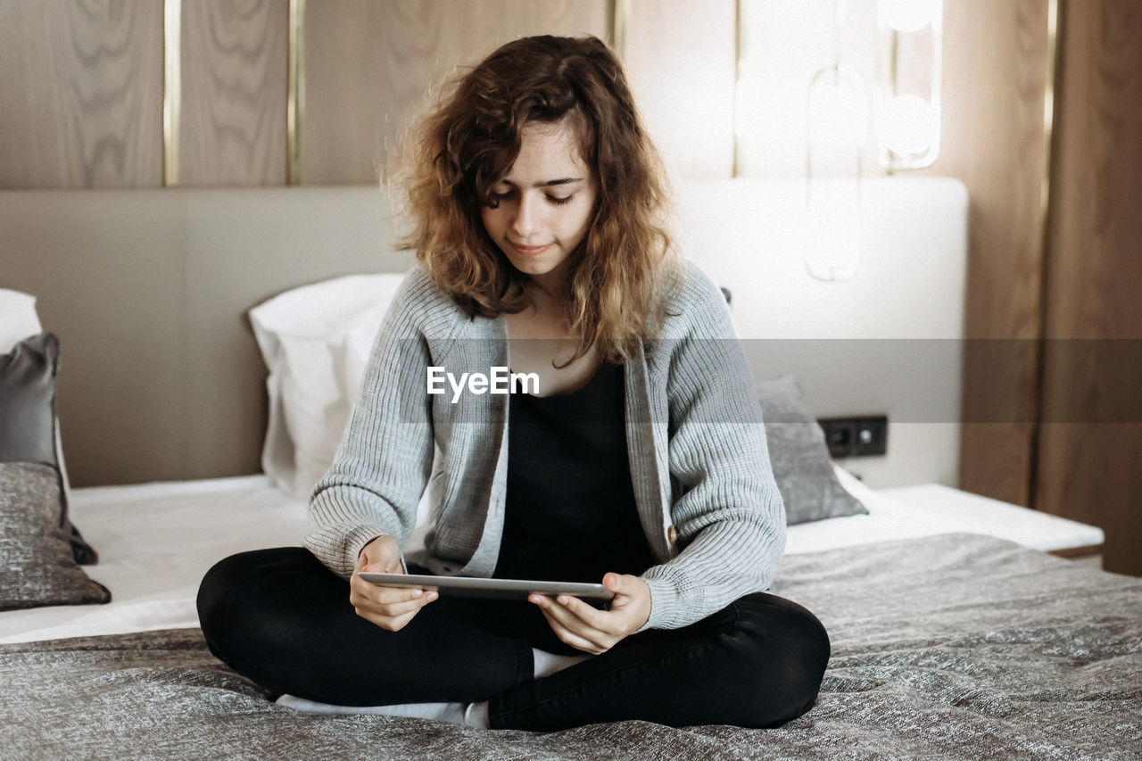 Teenager girl watching video or reading book on tablet on bed