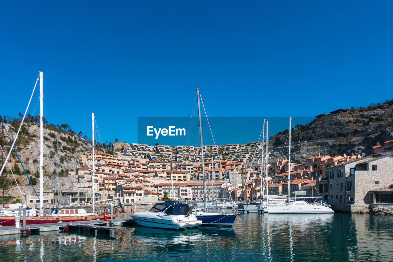 Sailboats moored at harbor against clear blue sky