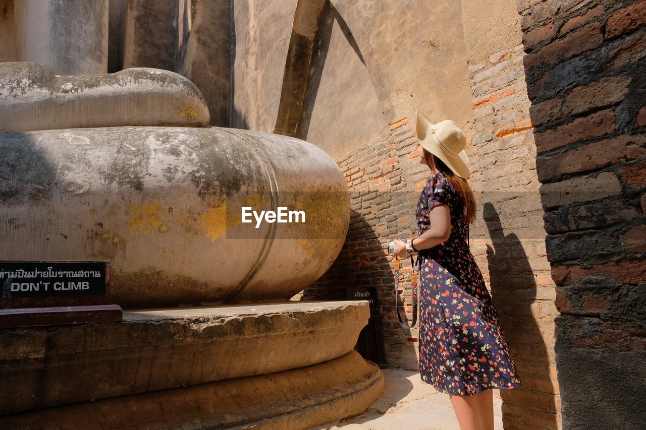 Side view of woman with camera looking at buddha statue 