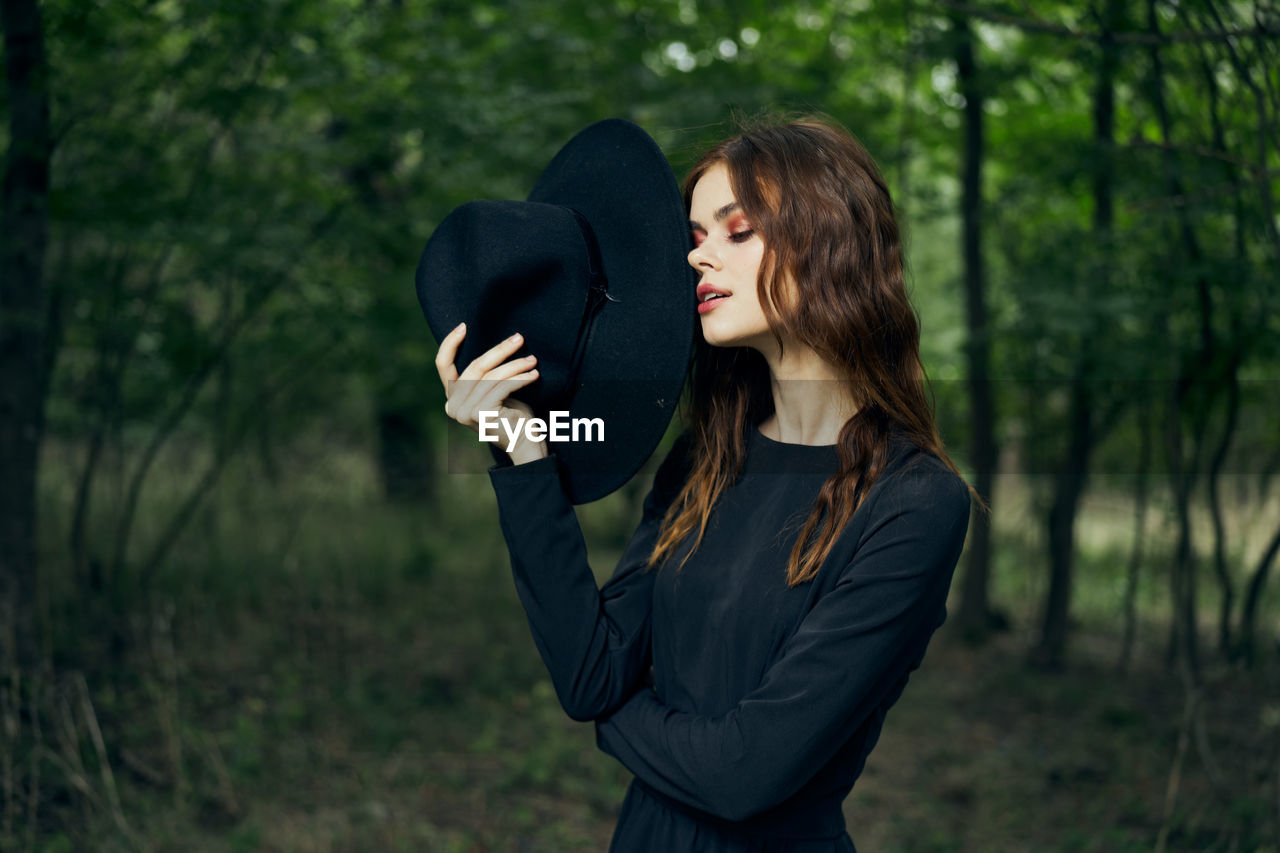 side view of young woman wearing hat standing in forest