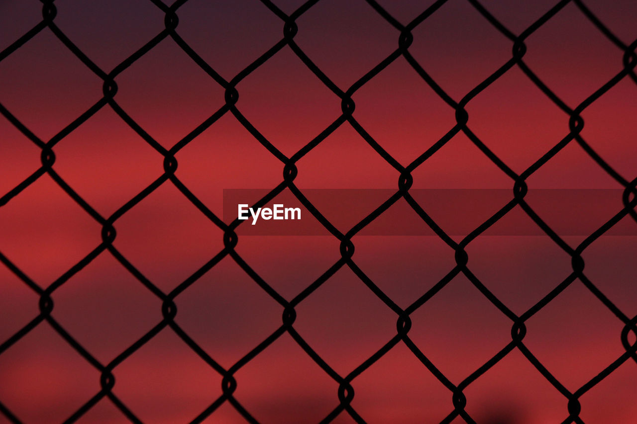 Full frame shot of silhouette chainlink fence against red sky during sunset