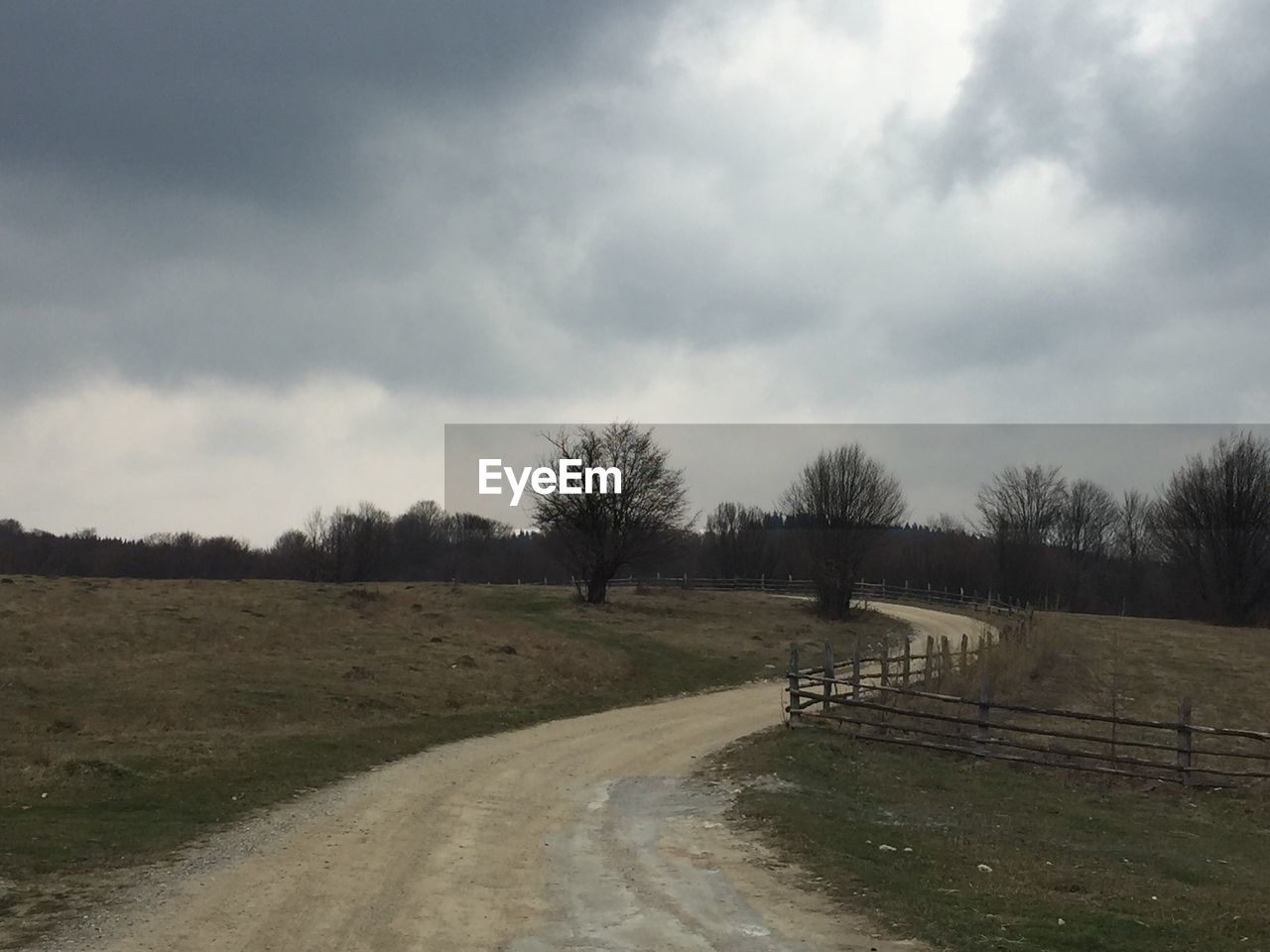 ROAD PASSING THROUGH FIELD AGAINST CLOUDY SKY