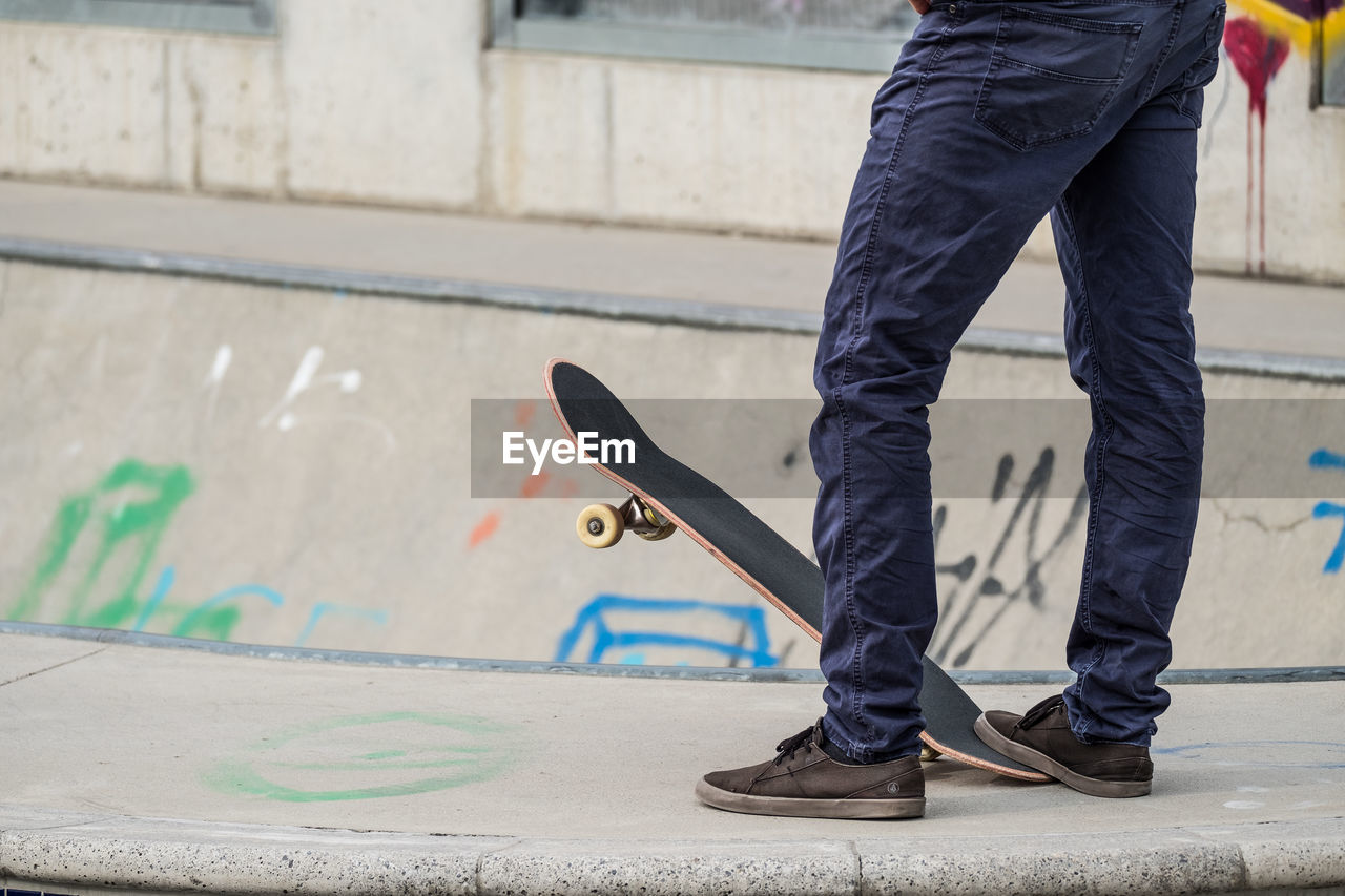 LOW SECTION OF MAN WITH SKATEBOARD ON STREET