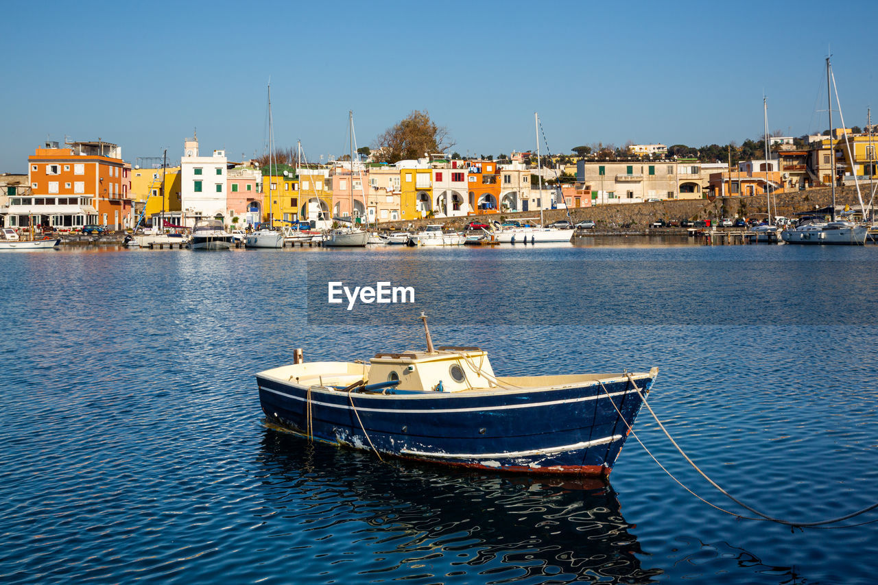 SAILBOATS MOORED ON SEA BY BUILDINGS AGAINST CLEAR SKY