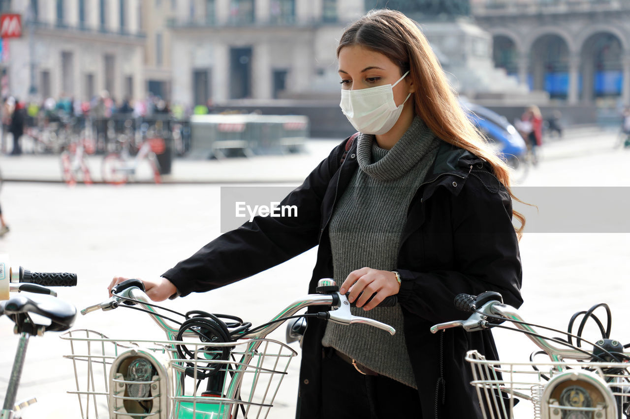 Young woman wearing mask holding bicycle standing outdoors