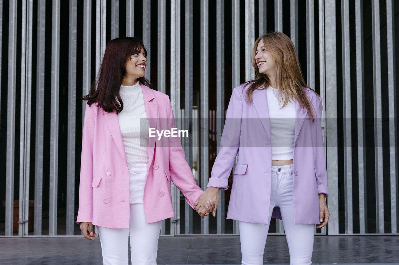 Smiling sisters holding hands while standing against wall