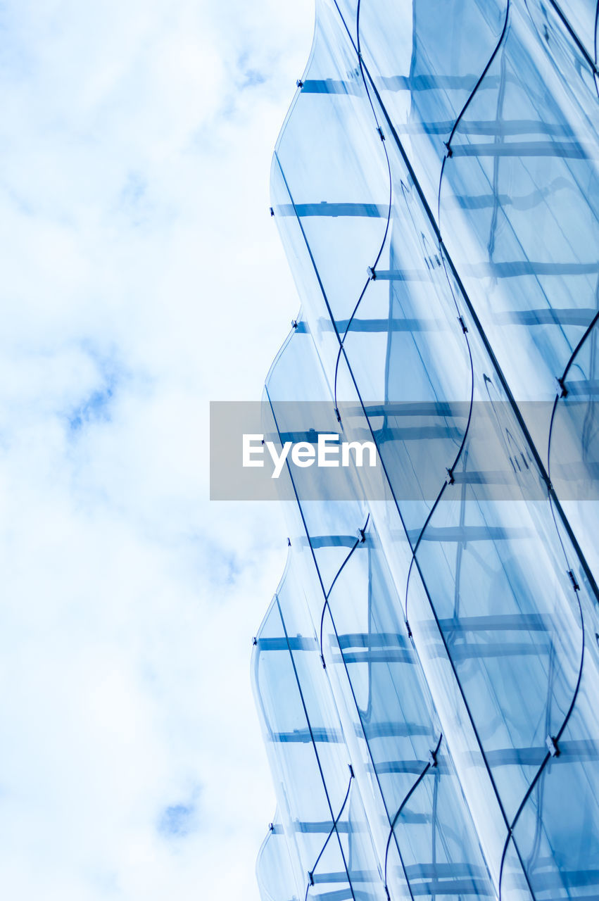 Detail of the wavy glass curtain wall facade of a nice modern building, sky and clouds reflecting