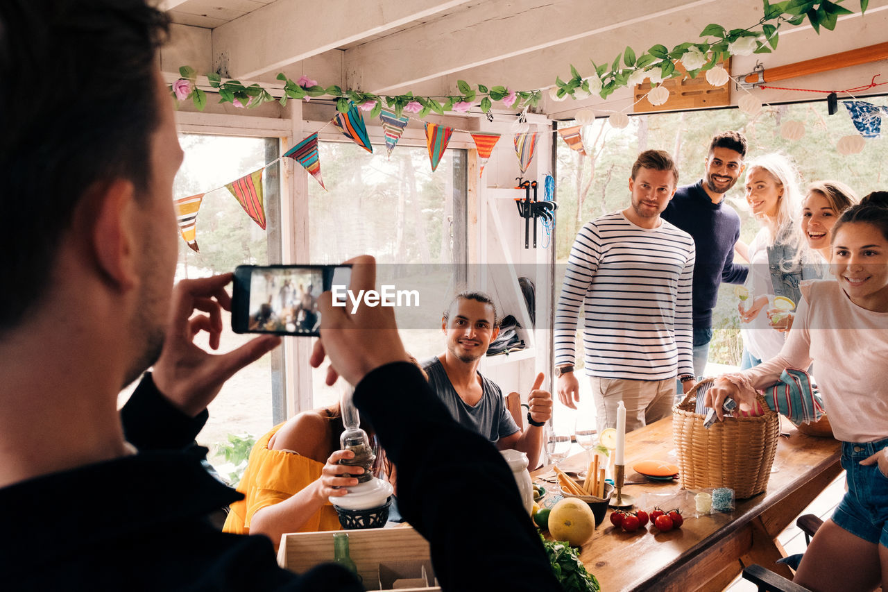 Man photographing friends on smart phone in cottage