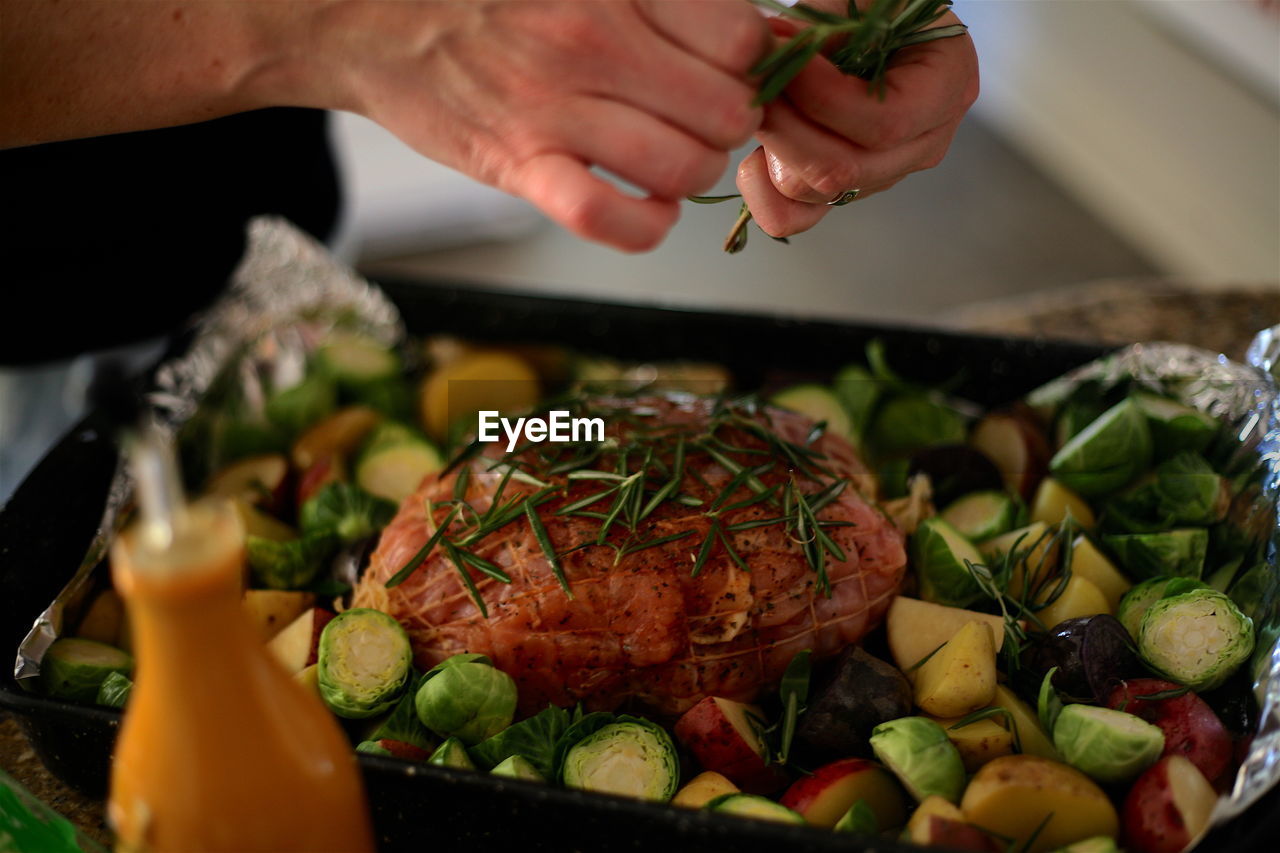 Cropped image of hands garnishing meat with rosemary in baking sheet