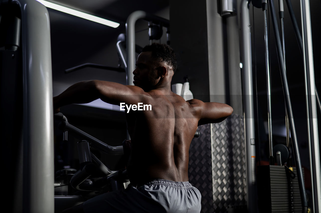 Shirtless african american man doing back exercises on a machine in the gym.