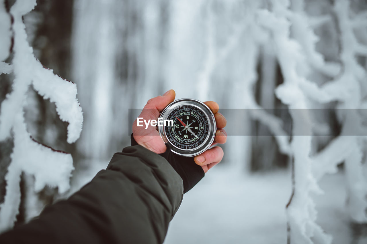 Cropped hand of man holding navigational compass during winter