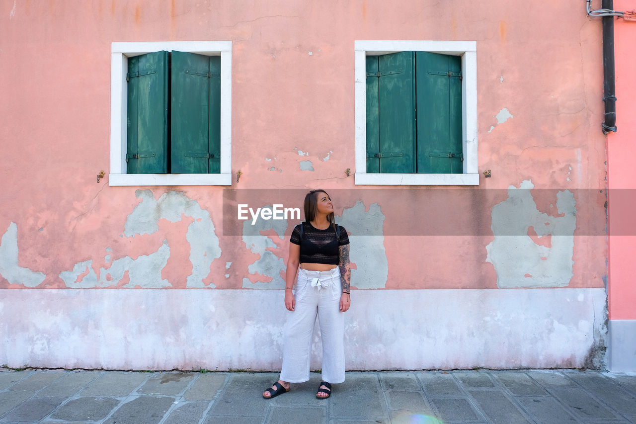 PORTRAIT OF WOMAN STANDING AGAINST DOOR OF BUILDING