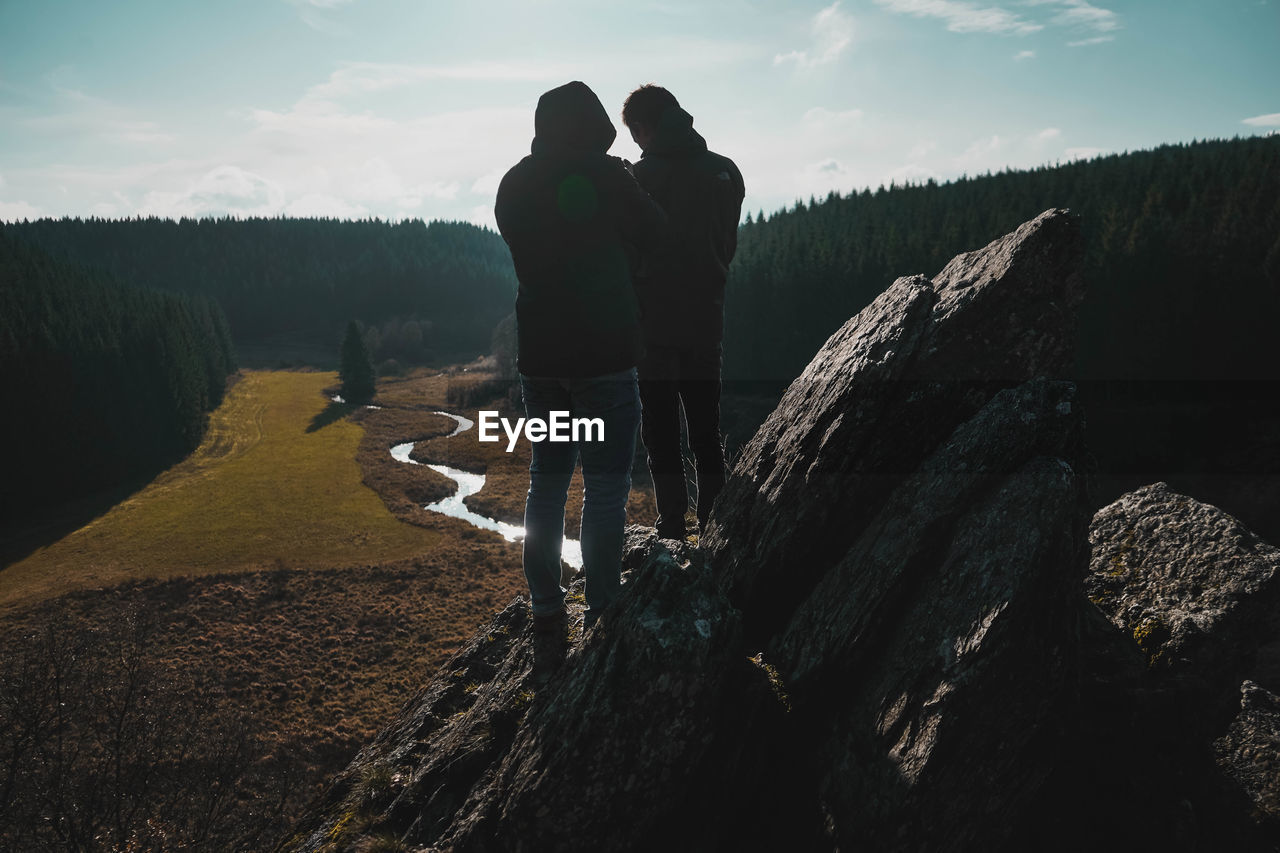 REAR VIEW OF FRIENDS STANDING ON ROCK