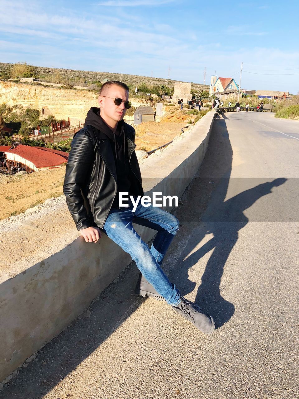 Young man sitting on retaining wall against sky