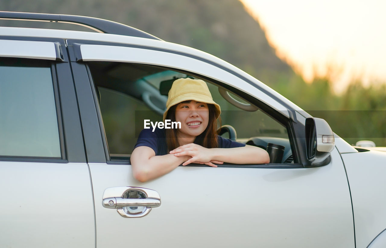 PORTRAIT OF A SMILING WOMAN SITTING ON CAR