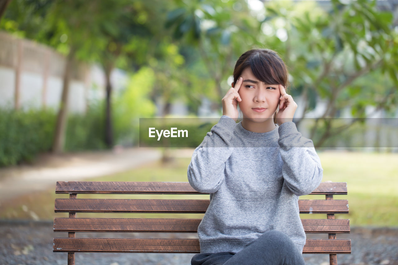 Young woman with headache sitting on park bench