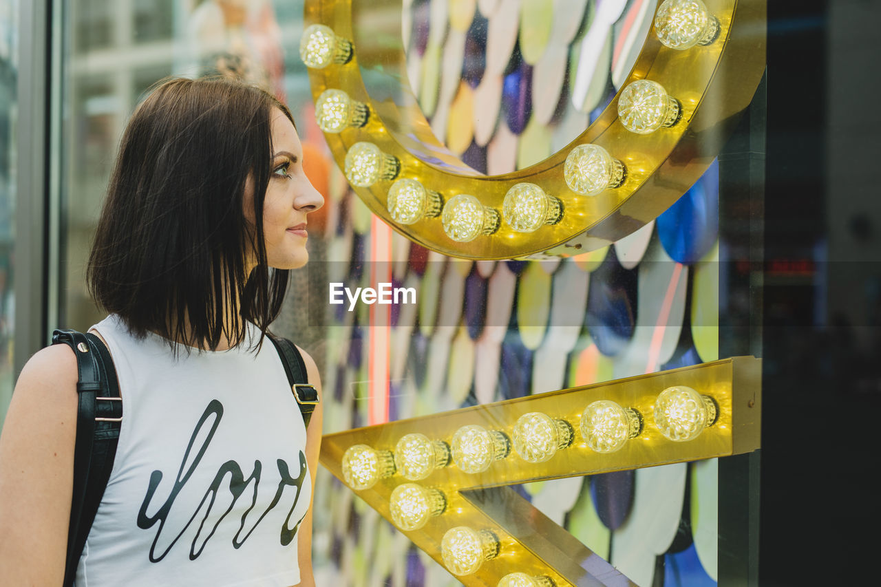 Young woman looking at window standing by store in city