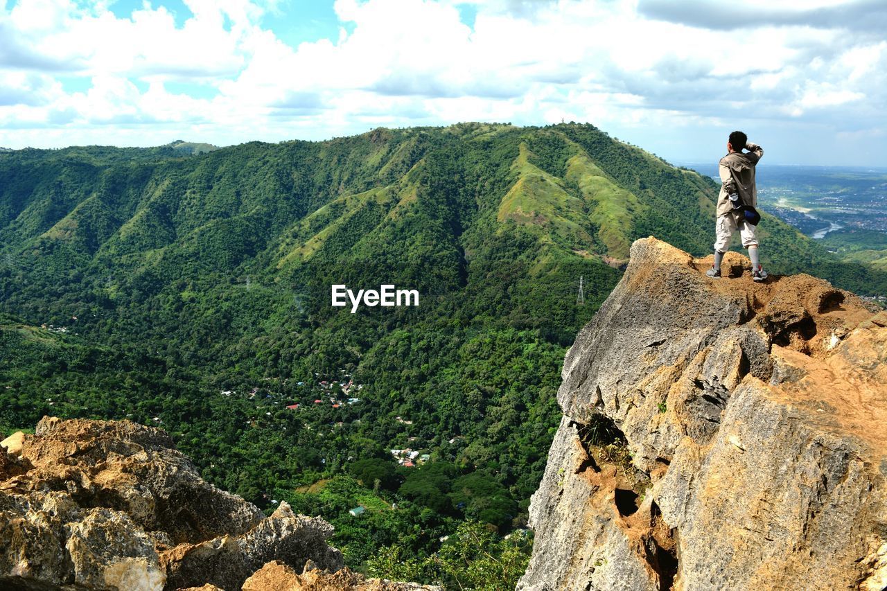 Rear view of man standing on rocky mountain against cloudy sky