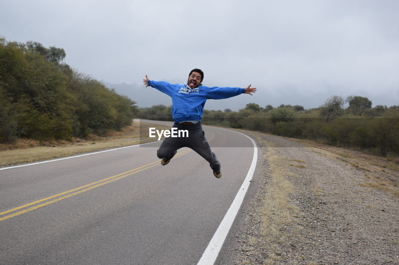 FULL LENGTH OF MAN JUMPING ON ROAD AGAINST SKY