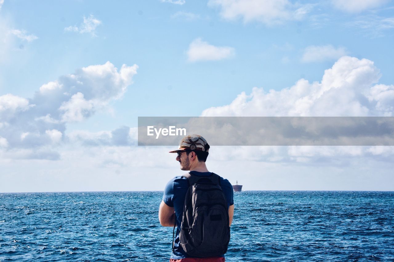 Rear view of man standing at beach against sky