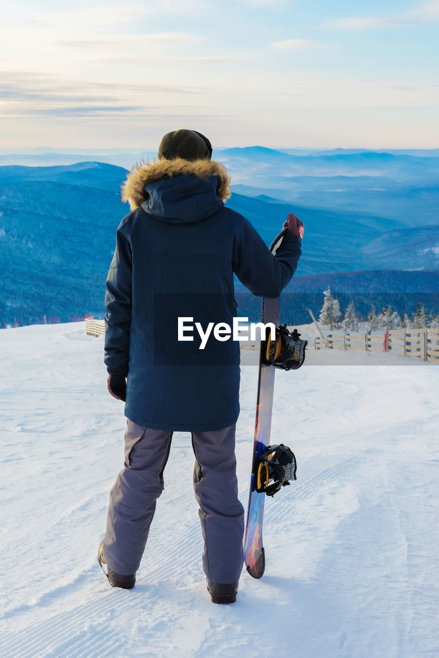 Rear view of man with snowboard standing on snow covered land