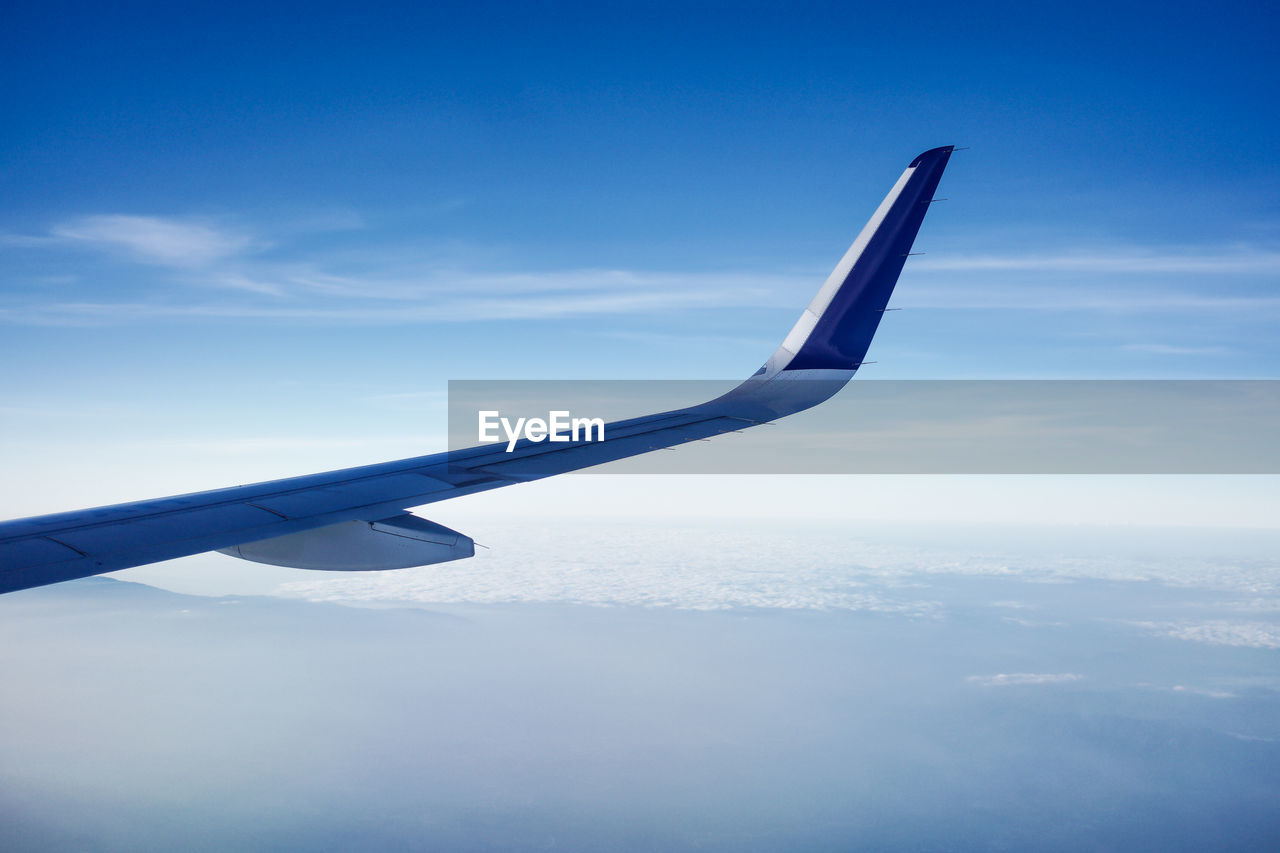 AIRPLANE FLYING OVER CLOUDS AGAINST SKY