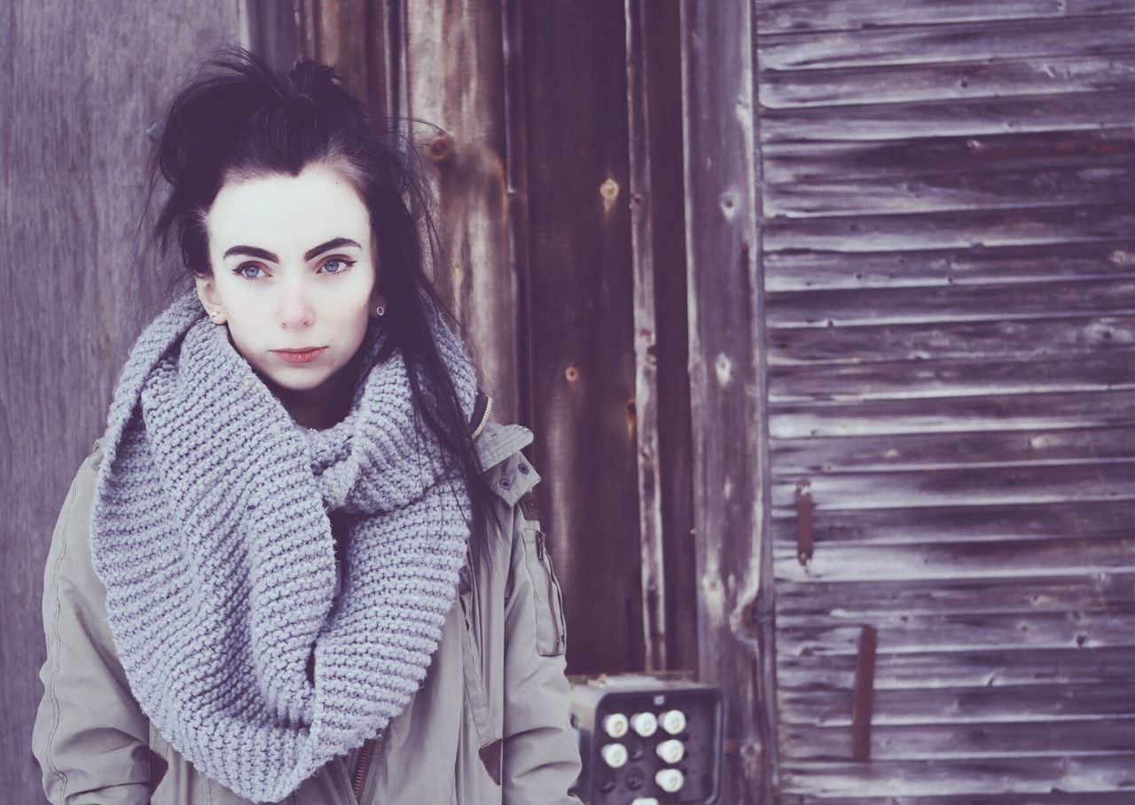 Thoughtful woman standing against wooden wall during winter