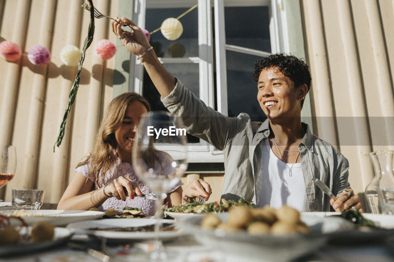 Happy young man enjoying food with friend during dinner party at cafe