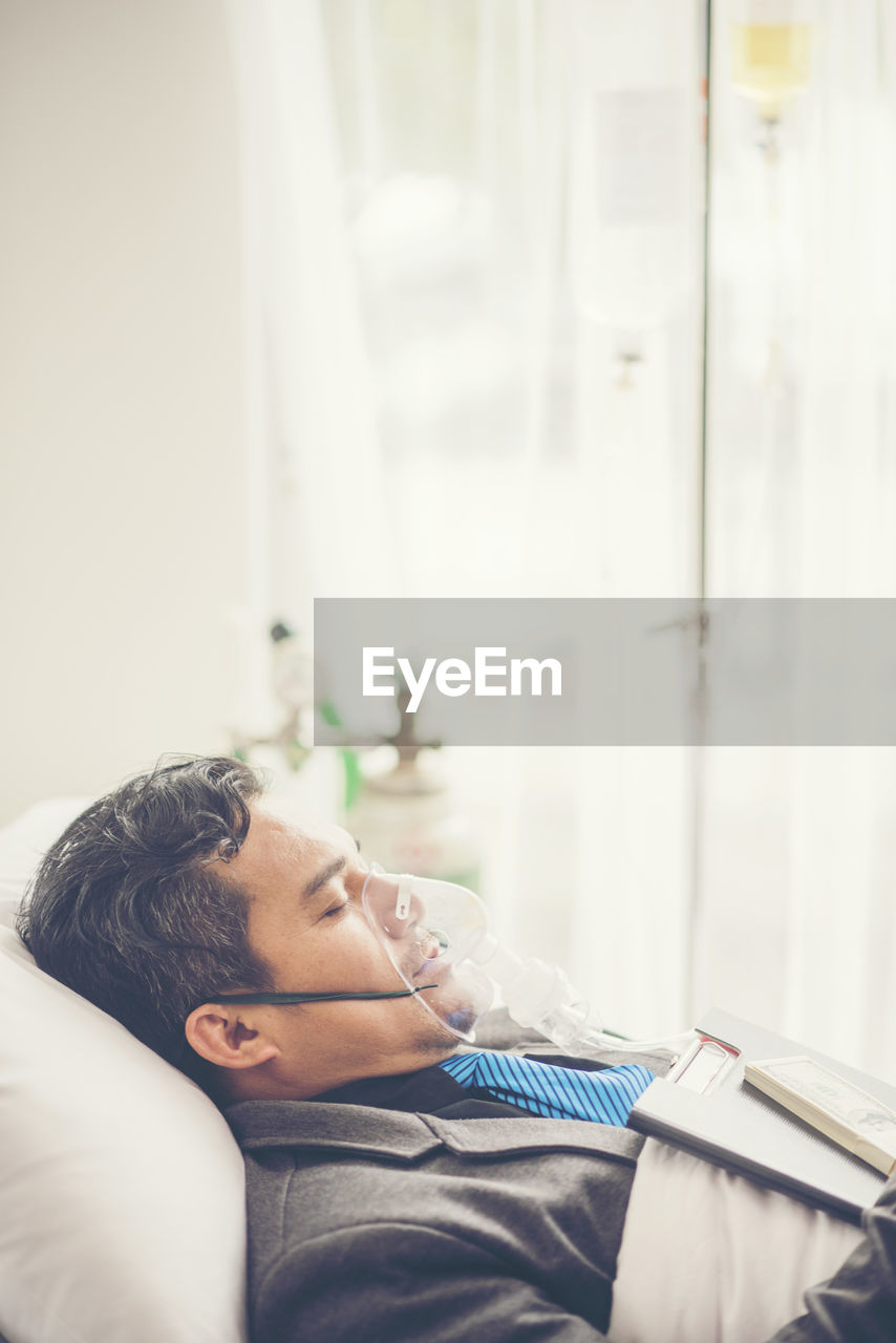 Side view of patient with file and currency lying on bed in hospital