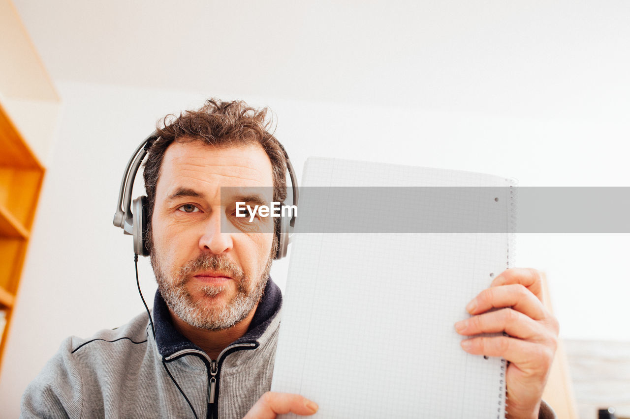 Mature adult male teacher showing note pad into camera in home schooling chat 