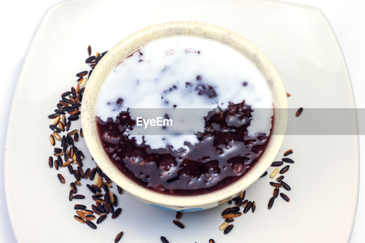 Thai black sticky rice wiht sweet coconut milk on top in white plate