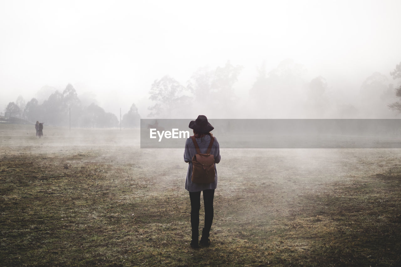 Rear view of woman standing on field during foggy weather