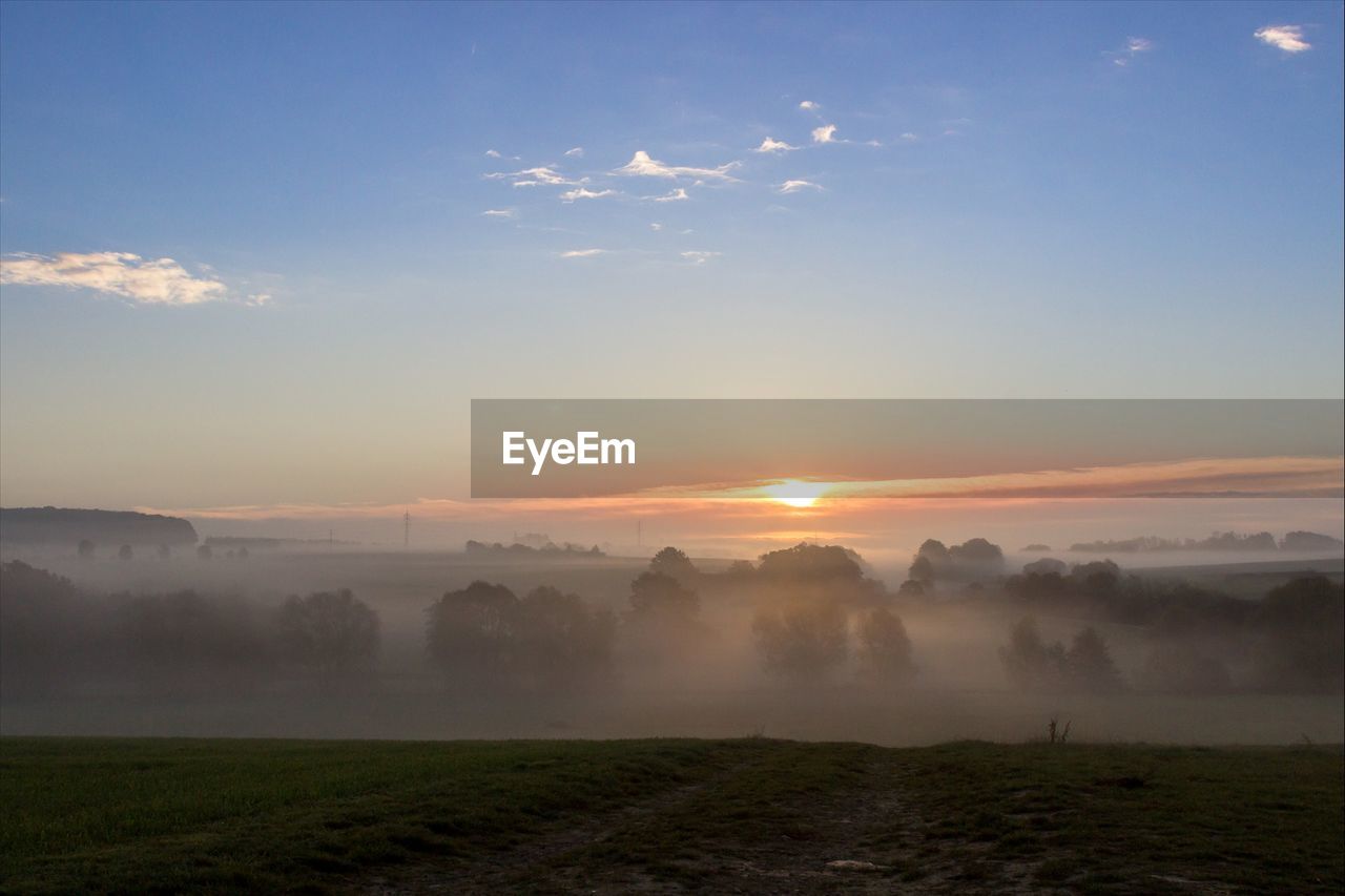 Scenic view of foggy landscape against sky during sunset