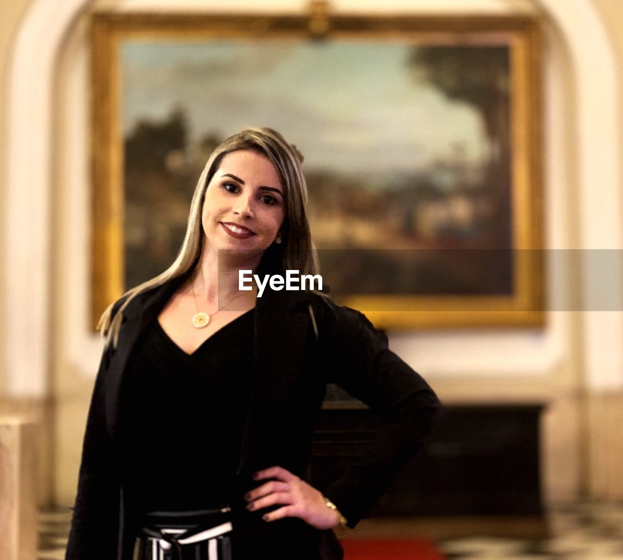 PORTRAIT OF A SMILING YOUNG WOMAN STANDING AGAINST A WALL