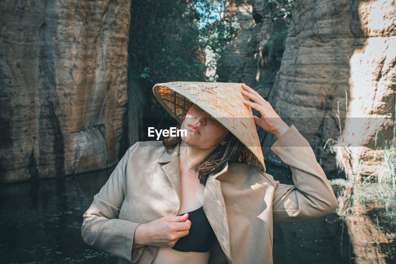 Young woman looking at camera, in nature wearing asian straw hat. 