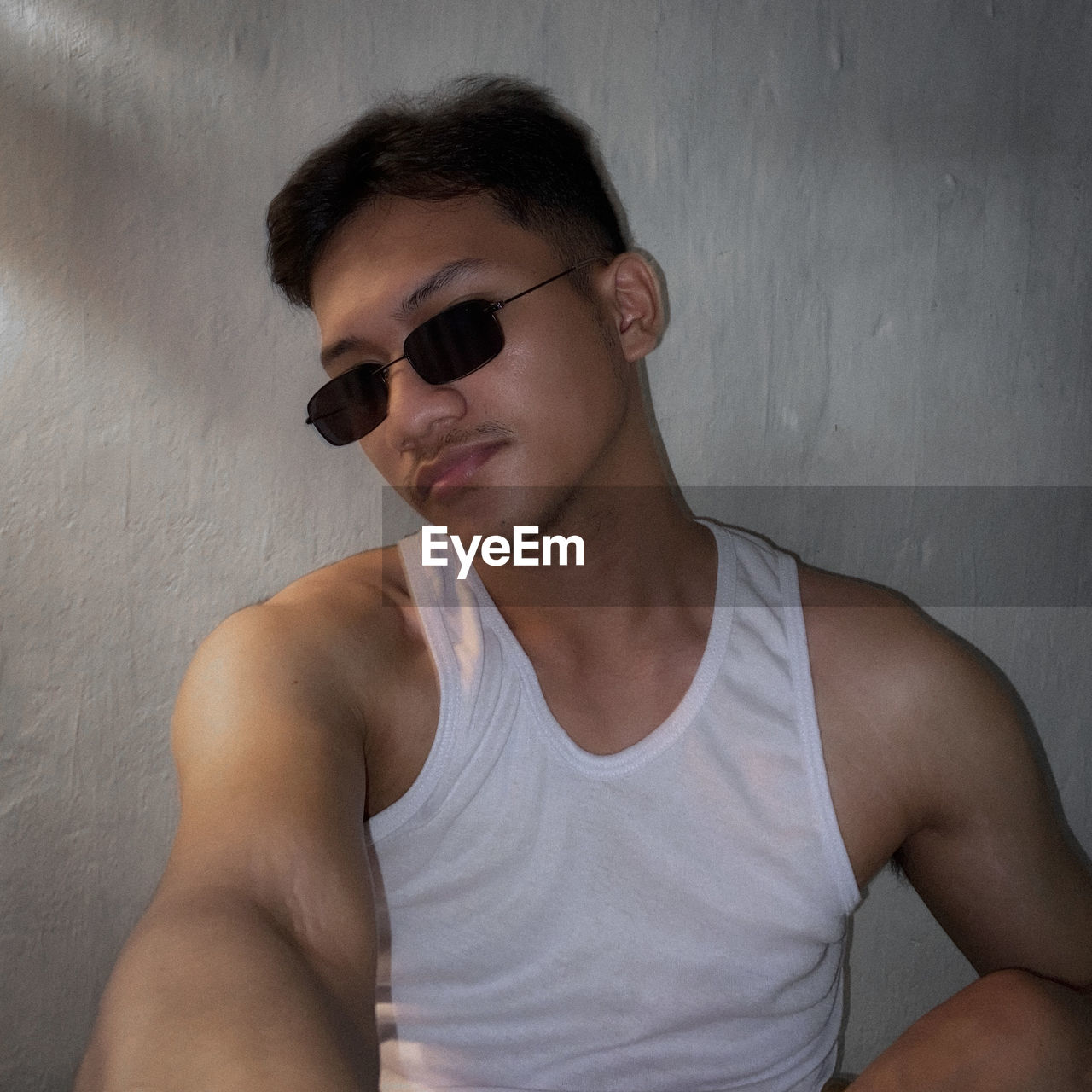 sunglasses, fashion, glasses, men, one person, portrait, human hair, hairstyle, young adult, barechested, adult, cool attitude, lifestyles, front view, person, waist up, wall - building feature, facial hair, arm, casual clothing, tank top, sleeveless shirt, t-shirt, indoors, gray, eyewear, vision care, human face, human mouth, leisure activity, clothing, limb, looking at camera, hand, headshot, photo shoot