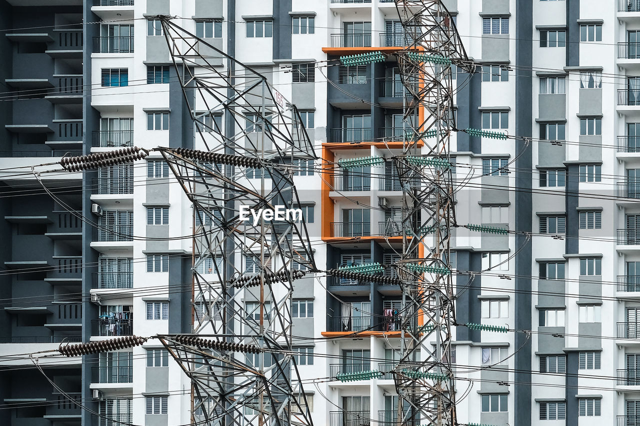 Low angle view of electricity pylons against building in city