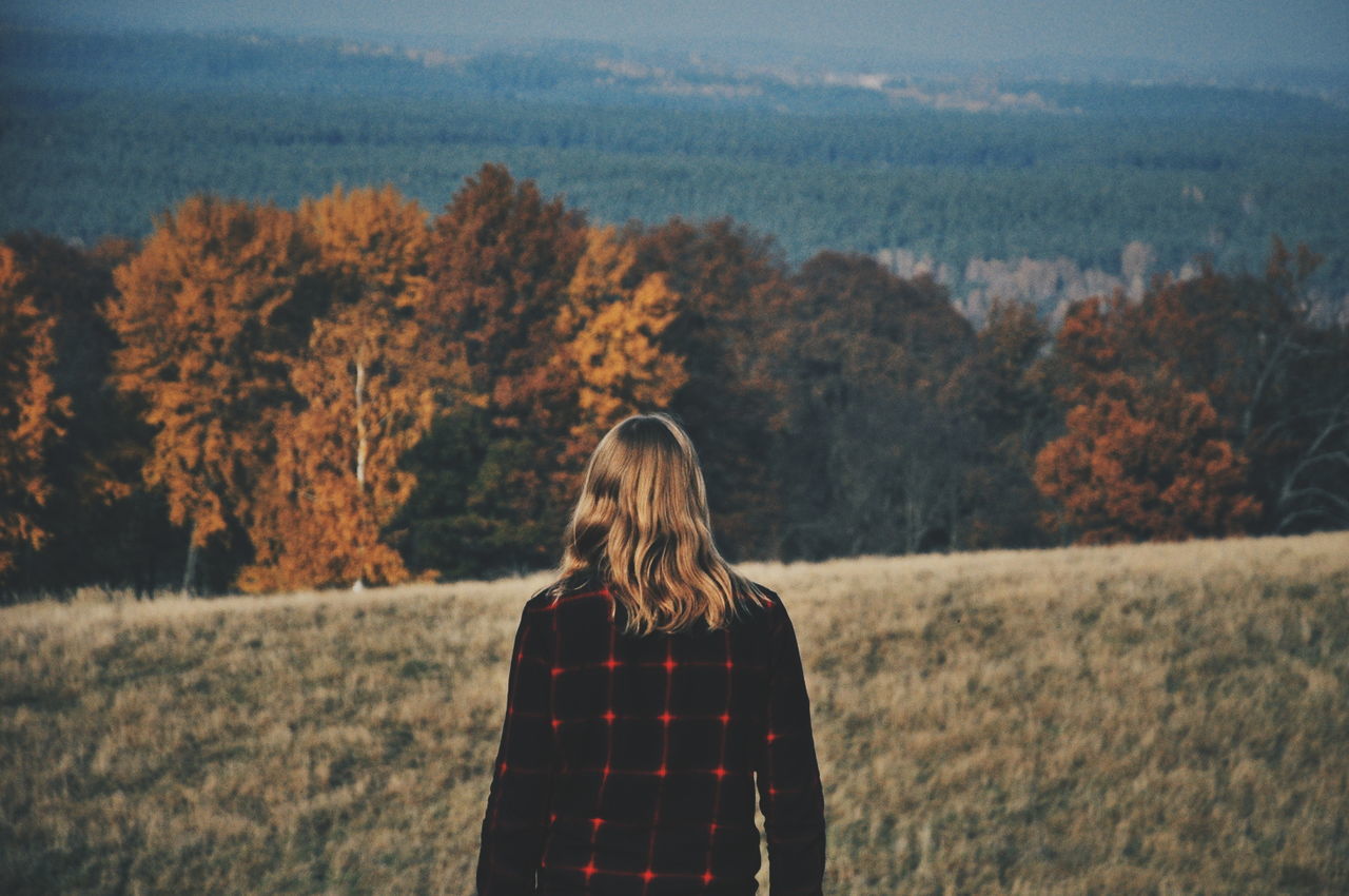 Rear view of man standing on field by autumn trees