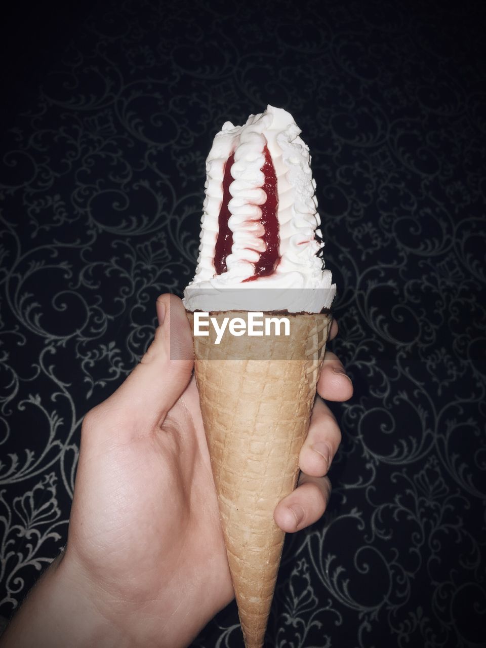 Cropped hand holding ice cream cone against wall