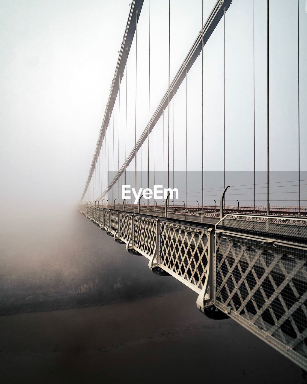 Suspension bridge leading towards sky during foggy weather