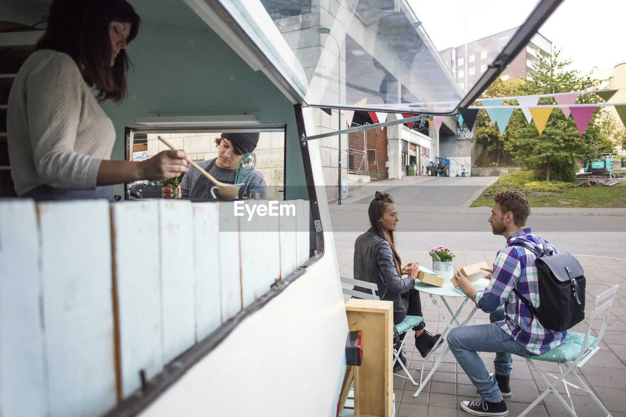 Owners working at food truck while customers sitting in background