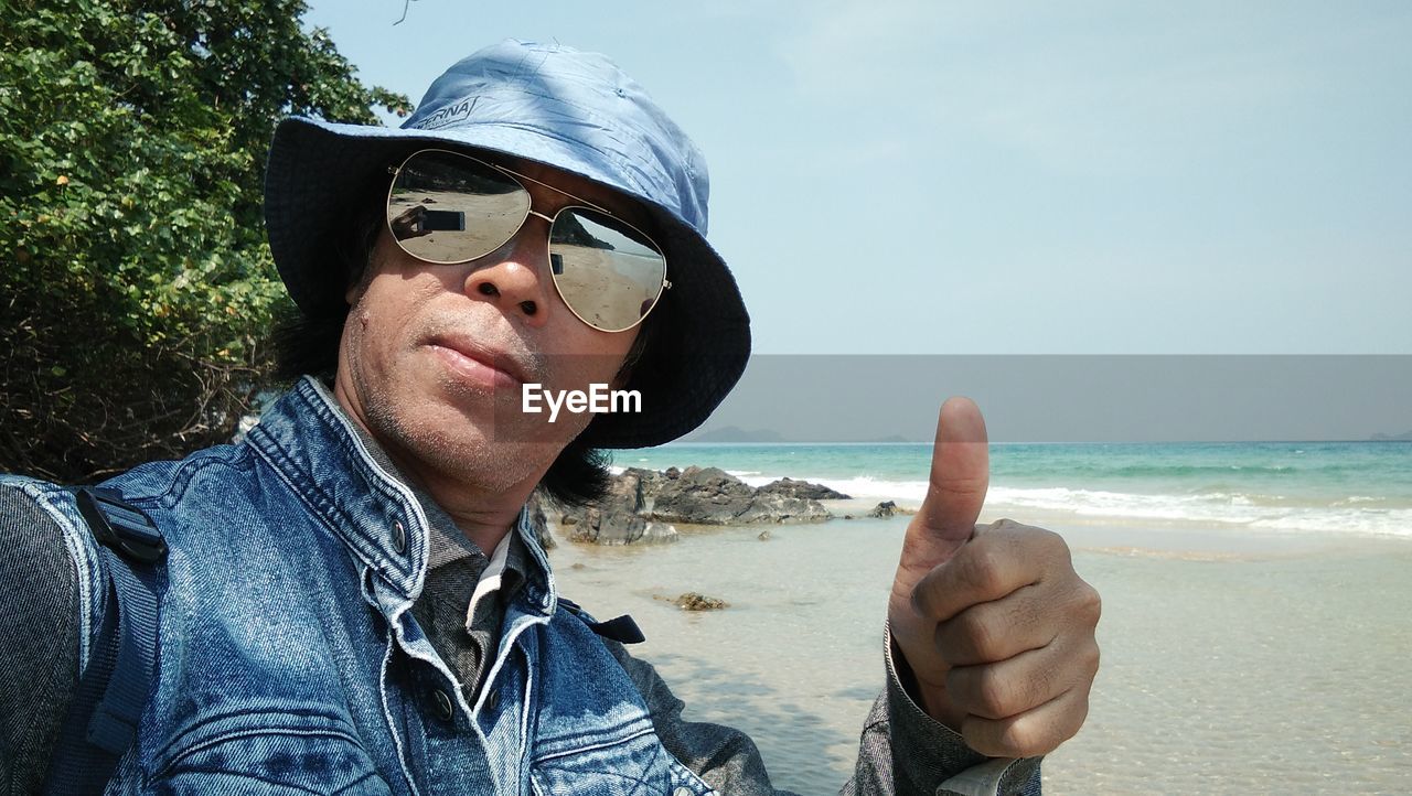 Man showing thumbs up sign at beach against sky