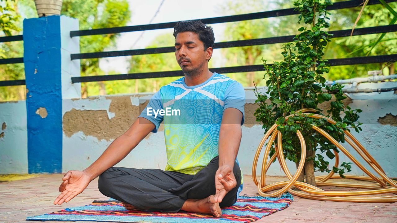 Attractive young indian man sitting in yoga pose at home. practicing yoga in the every morning.