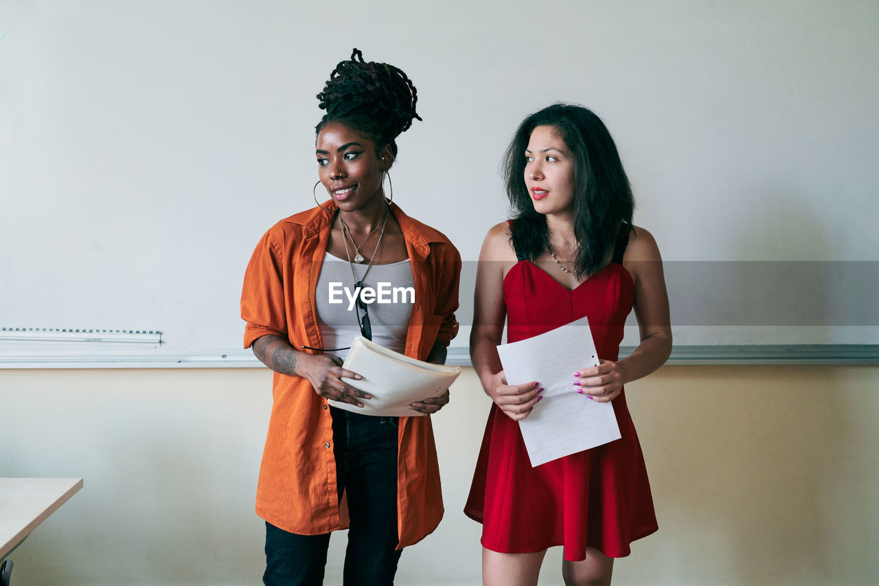 Female teachers looking away while holding documents in classroom