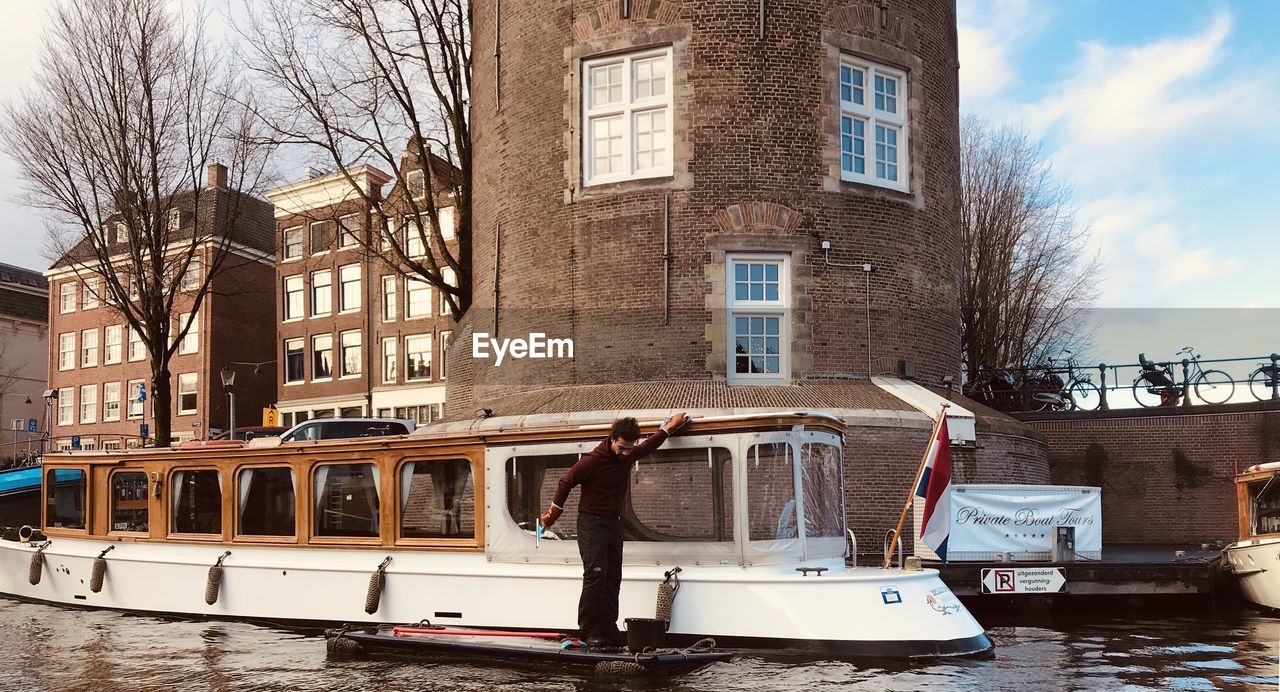 REFLECTION OF BARE TREES IN CANAL AGAINST BUILDINGS