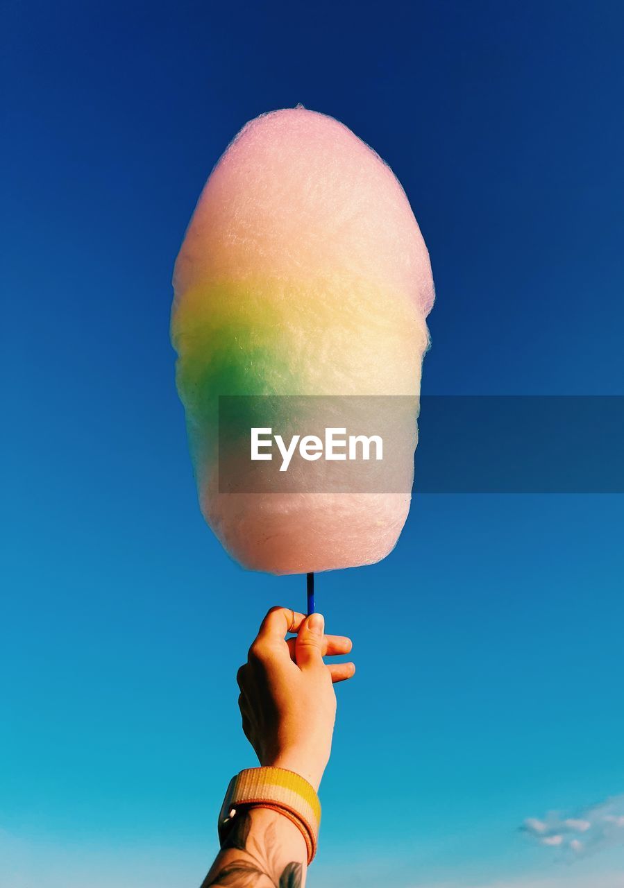 Cropped hand holding cotton candy against blue background