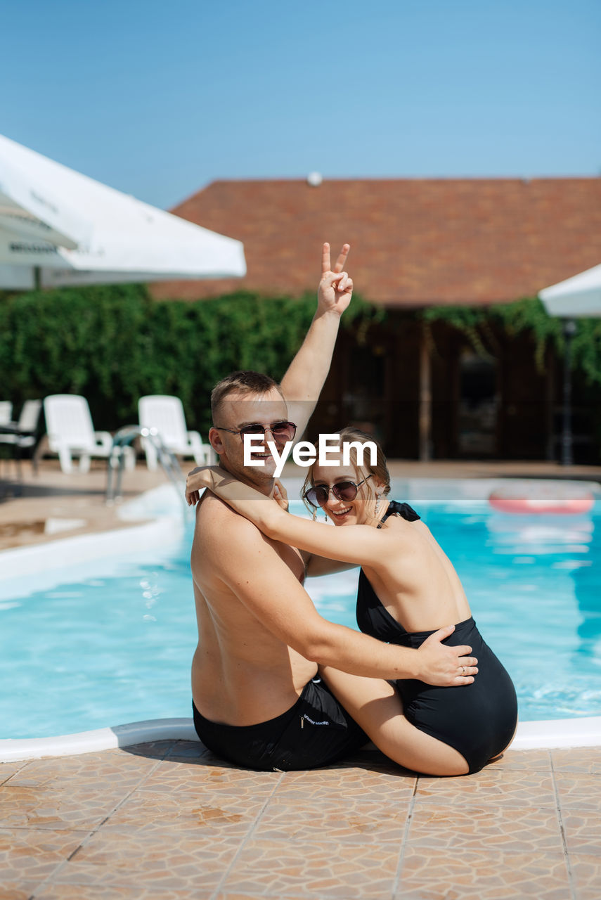 swimming pool, adult, two people, happiness, women, water, men, togetherness, emotion, poolside, swimwear, smiling, vacation, young adult, enjoyment, positive emotion, summer, trip, swimming, holiday, nature, lifestyles, clothing, cheerful, leisure activity, relaxation, fun, love, female, bonding, arm, day, limb, tourist resort, portrait, glasses, human limb, sunglasses, outdoors, sunny, sunlight, friendship, arms raised, travel destinations, full length, carefree, travel, fashion, luxury, architecture, hotel, food and drink, romance, sky, bikini, looking at camera, human leg, wealth