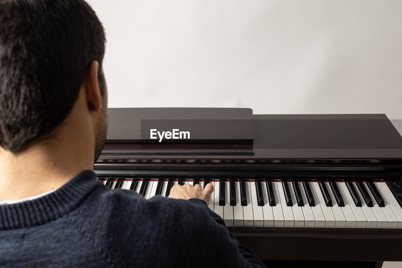 REAR VIEW OF MAN PLAYING PIANO AT HOME