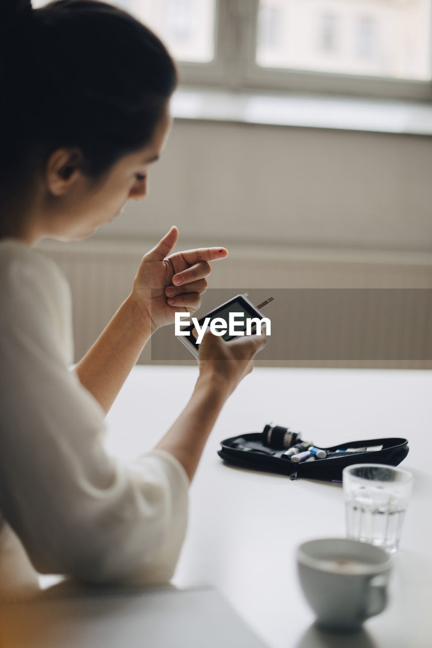 Close-up of woman checking blood sugar level in glaucometer while sitting at table